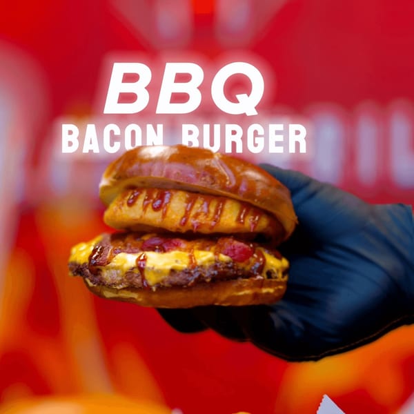 A hand in a black glove holds a Blazin’ Grill BBQ Bacon Burger with melted cheese and sauce.